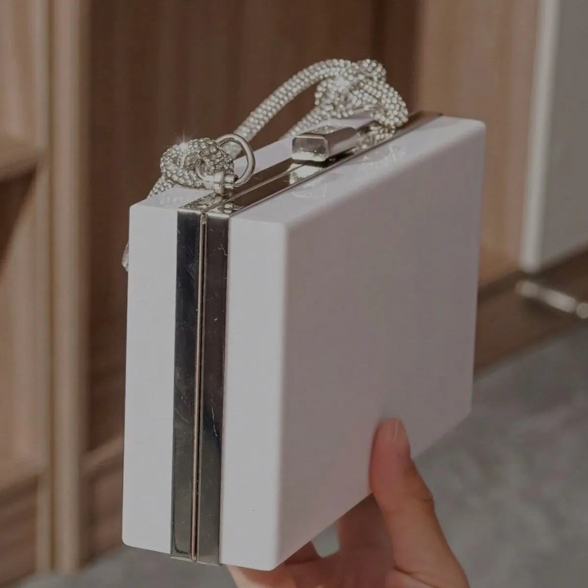 Women's white acrylic clutch features a distinctive rhinestone-encrusted top handle